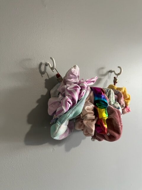 Scrunchies being held on a small bungee cord between wall-mounted cup hooks