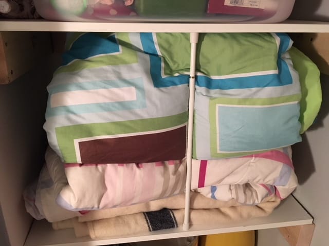 A tension rod placed vertically between two closet shelves to keep a pile of blankets from toppling out onto the floor